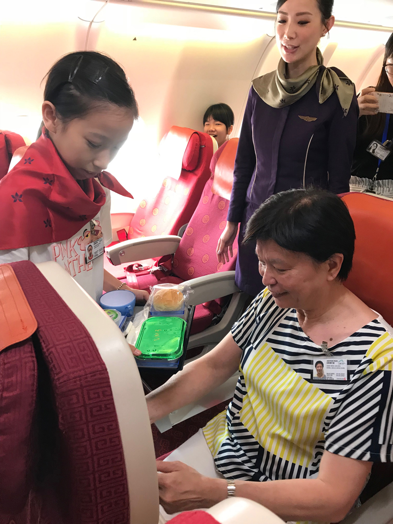 學員扮演機艙服務員，嘗試為乘客送餐，其中為兒童發展基金督導委員會委員黃何明雄博士。